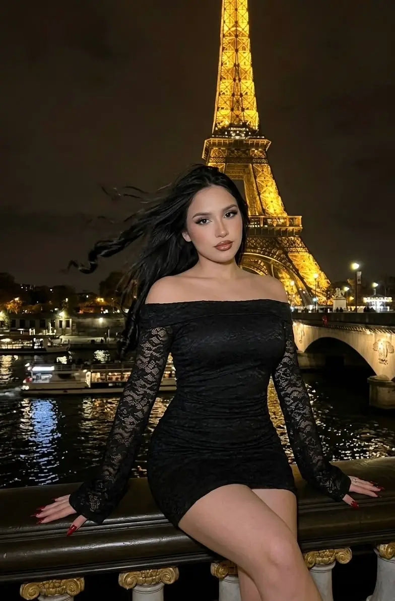 Outfit del día (mujer): vestido negro de encaje de hombros descubiertos frente a la torre Eiffel
